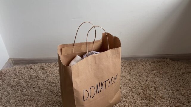 Person donating clothes in a paper bag for charity, practicing decluttering, sorting, and recycling old items for a minimalist lifestyle at home