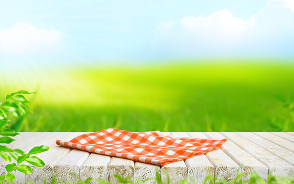 Selective focus.Red fabric placemat cloth on white rustic wood top on blur fresh greenery field