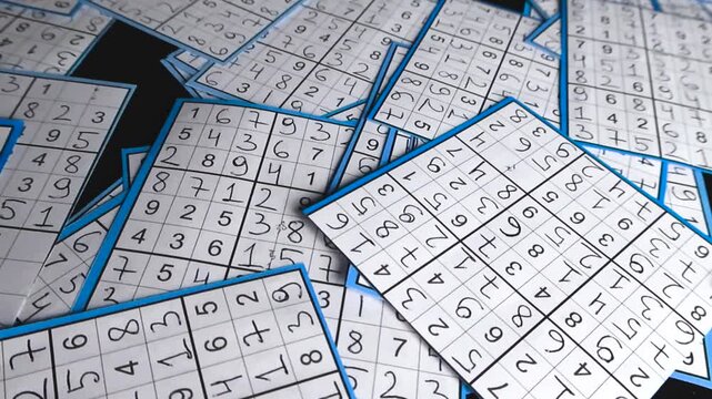 Multiple paper cutouts of solved sudoku puzzles randomly scattered on a black studio background. This logical brain teaser represents a popular mind game for training concentration and memory