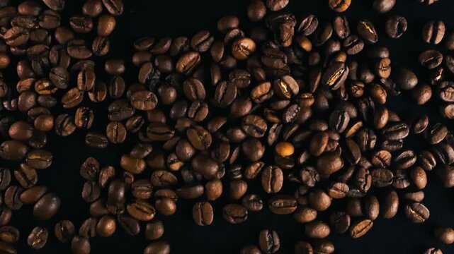 Top down view of aromatic dark roasted coffee beans moving and shifting on a black background, showcasing the rich texture and color of the quality arabica or robusta beans