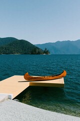 Fototapeta premium Wooden canoe resting on a beige dock at a mountain lake with forested hills for poster background and nature travel promotion