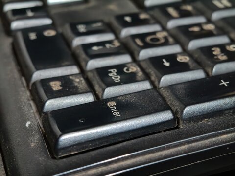 Extreme close up of a black computer keyboard with the Enter key and surrounding keys showing dust and wear