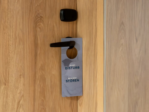 A do not disturb sign hanging on a wooden hotel room door handle, conveying a message of privacy, quiet, and guest comfort during a stay at a modern travel lodging establishment