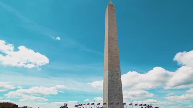 Monument Obelisk Timelapse with Waving National Flags and Tourists Walking Against a Blue Sky in 4k Resolution Capturing a Low Angle Perspective of a Grand Stone Pillar