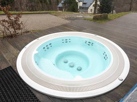 A round outdoor hot tub sits on a wooden terrace, offering a serene space for relaxation in a natural garden setting, highlighting luxury leisure and wellness during spring holidays