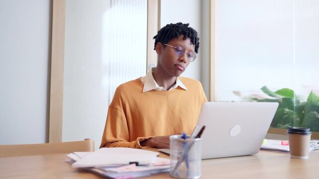 Stressed African American male freelancer feeling tired and rubbing forehead while working on laptop in office