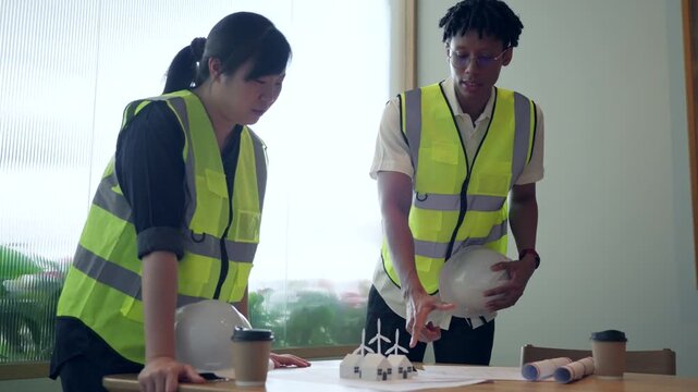 Engineers planning renewable energy project with eco house models and wind turbines.	