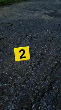 Yellow evidence marker with the number two placed on a wet, muddy road at a crime scene, indicating the presence of important clues like tire tracks and footprints left in the dirt