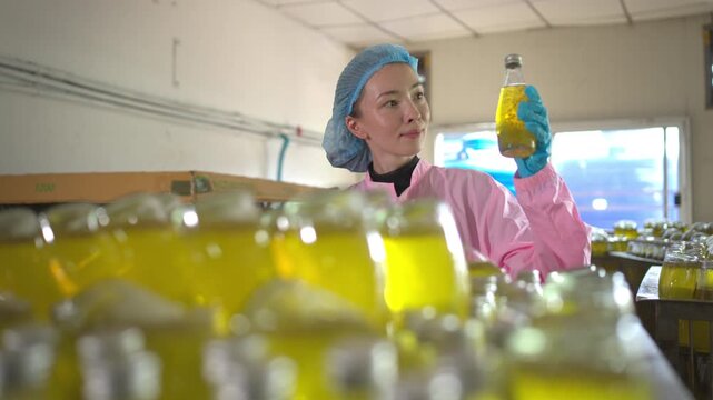 The female employee is giving the final check of the beverage bottles on the bottling shelf before packing them into boxes and passing them on to the distributor