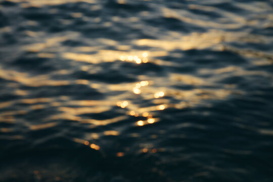 Abstract blurred golden sunset light reflections on dark blue ocean waves background