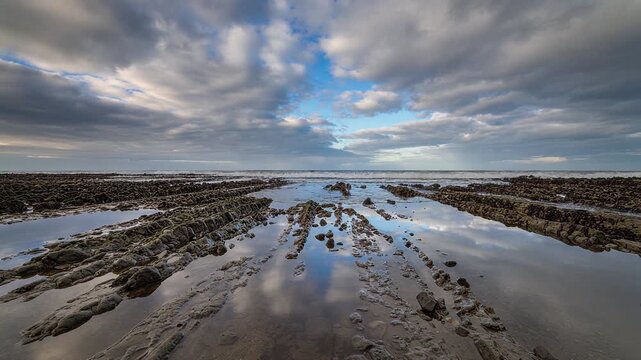 Beach loop tide pools shimmer with sky reflections and gentle waves lapping across sandy beach