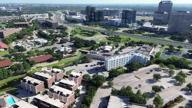 Low rise townhomes border corporate parking facilities near major highway interchanges linking local businesses in Las Colinas, Irving, Texas. High density commercial glass towers define skylines