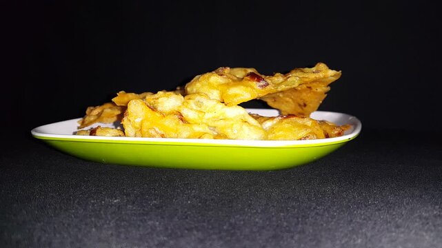 Crispy Indonesian Vegetable Fritter Bakwan. A close-up shot of freshly fried Indonesian vegetable fritters, known as Bakwan, served on a modern plate against a dark background.