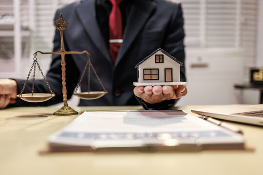Businessman holding a small house model beside scales of justice in an office, real estate law, property disputes, and legal advice.