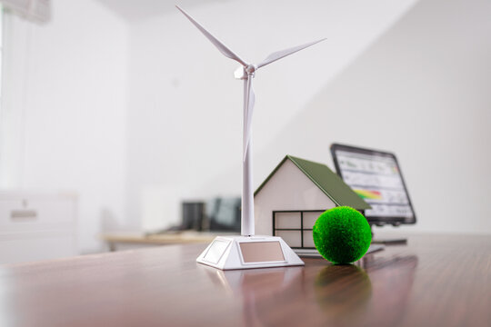 Miniature wind turbine, house model and tablet with charts on a desk, renewable energy, home power, and clean technology concept.