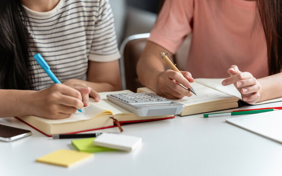 Asian female students writing in notebook while preparing for upcoming education assignment
