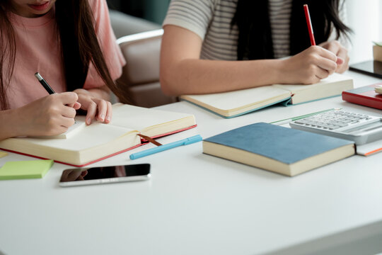Asian female students writing in notebook while preparing for upcoming education assignment