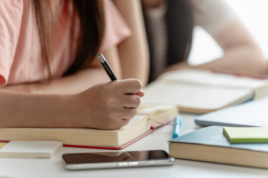Asian female students writing in notebook while preparing for upcoming education assignment