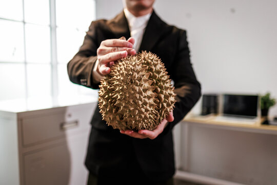 Man in suit holding a durian fruit in an office room, close up with soft background blur
