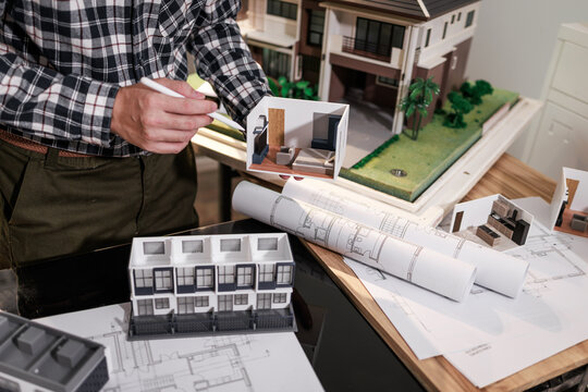 Architect reviewing a house model with floor plans and design samples on a desk