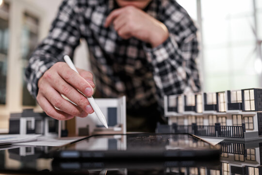 Person using a stylus and tablet beside a building model, working on home design and planning in an office setting