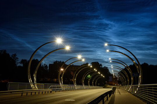 Valmiera Latvia-July 16,2026-Modern illuminated bridge at blue hour with glowing street lights, dramatic clouds, and an empty road creating a striking urban perspective.