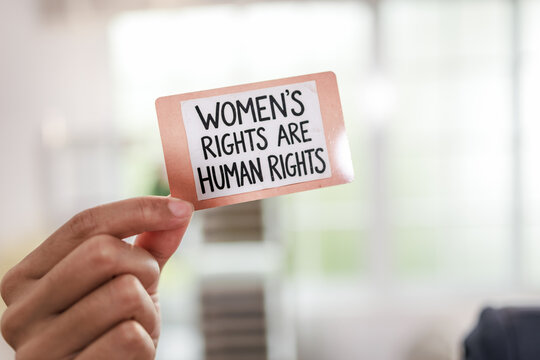 Hand holding a small protest card with womens rights are human rights message on a soft blurred background