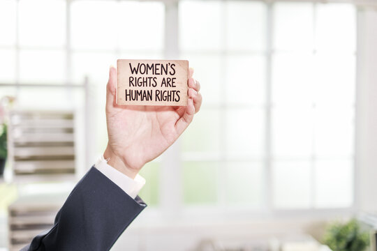 A hand holding a sign with the message women's rights are human rights in a bright office setting