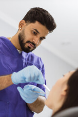 Fototapeta premium A male dentist in blue scrubs and gloves performs a dental examination on a patient with specialized tools