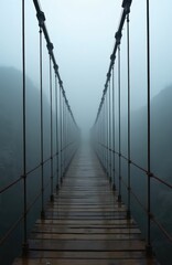 Obraz premium Old suspension bridge with rusted cables disappears into thick fog and mist. Wet wooden planks lead over a dark abyss. Moody atmosphere, sense of mystery and isolation. Cinematic perspective.