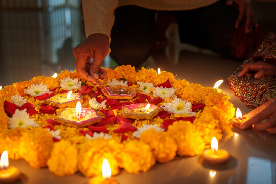 Cropped hands arranging burning clay diyas on floral marigold rangoli for Diwali festival