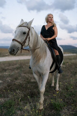 Fototapeta premium Woman horse riding elegant blonde across a grassy plain under a dramatic cloudy sky