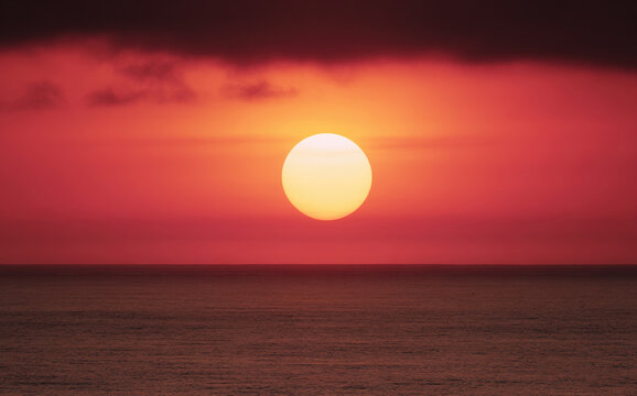 Bright sun setting over the ocean with a colorful sky in the background during evening time