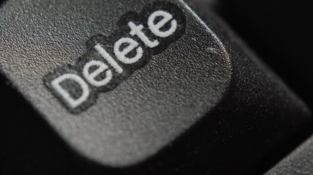 Close-up of a finger pressing the Delete key on a computer keyboard. Concept of removing data, correcting mistakes, cancellation, and technology.