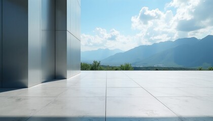 Obraz premium Empty concrete patio floor with modern metal building wall. View of green mountain valley landscape under bright blue sky with white clouds. Urban terrace space features tile pavement surface for