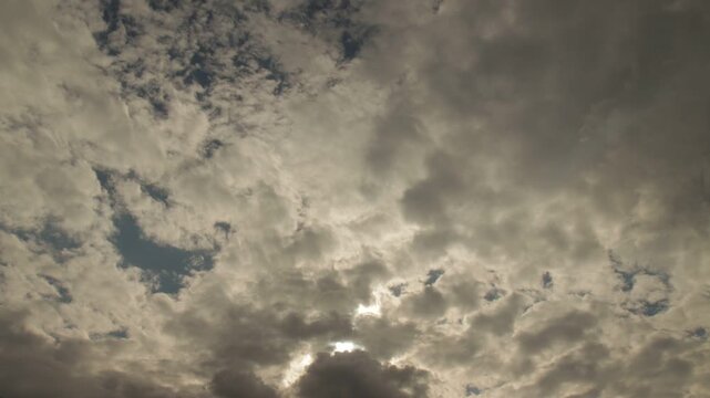 Timelapse of broken layered clouds moving around the sun in a bright daytime sky