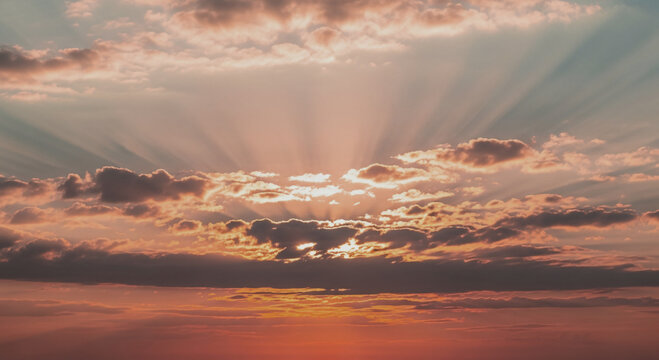 Beautiful sunrise with sun rays peeking through fluffy white clouds in sky