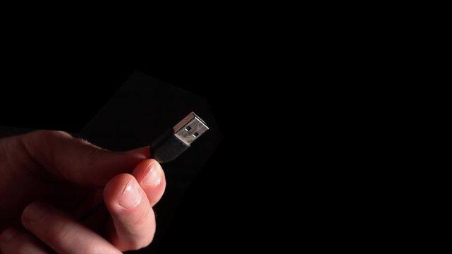 A hand holds one USB connector on a black background