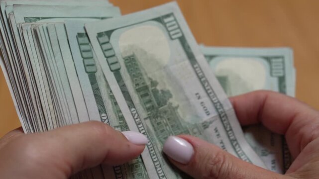 Money, cash, counting, female hands counting stack of hundred dollar banknotes indoors demonstrating wealth and financial success with crisp bills for investment concept