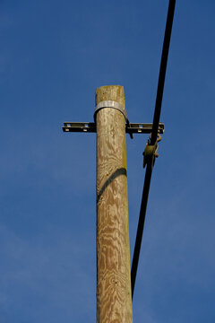 A weathered wooden utility pole with a metal crossarm and cable stands against blue sky