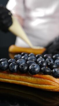 Final touch concept in cooking. Professional dessert production. Fresh cream tartlets on baking tray in pastry kitchen with chef making desserts using creamy filling and berries. Vertical 4 k video