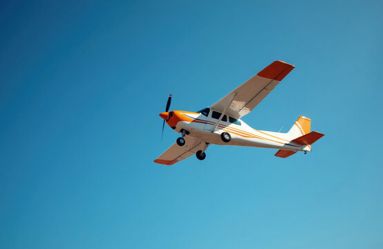Small white and orange propeller plane flies against clear blue sky. This aircraft is suitable for private flights, tours or cargo transport. Modern aviation.