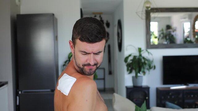 Man applying heating patch to relieve severe shoulder blade and back pain