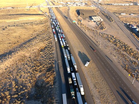 Aerial drone photograph of heavy truck traffic on a major interstate highway with long line of freight vehicles transporting cargo. Transportation, logistics, supply chain, infrastructure and commerci