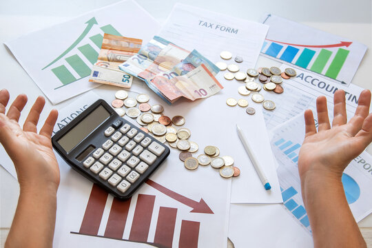 A businessman's hands, with a frustrated sign, are spread over financial documents and graphs on an office desk. Budgeting, taxes, rising costs, financial stress, business economic crisis
