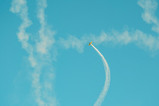Portugal Oeiras Air Show. A pilot maneuvers an aircraft in the sky, creating a smoke trail that arches through the air during an airshow. This takes place on a clear day, showcasing flying skills.