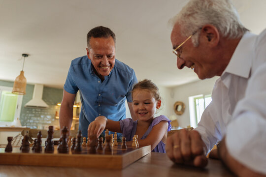 Multi generational male family teaching girl playing chess