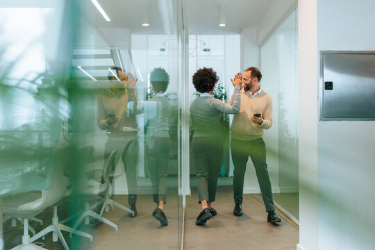Business colleagues high fiving celebrating teamwork success in office