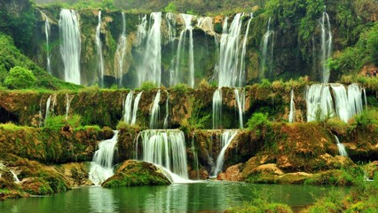 Spectacular multi-tiered waterfall cascading down mossy rock cliffs into a calm pool. © Danan