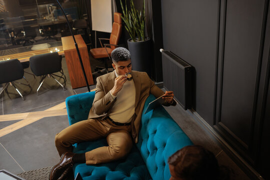 Businessman drinking coffee and using tablet in office lounge